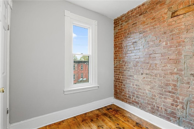 spare room with hardwood / wood-style flooring and brick wall