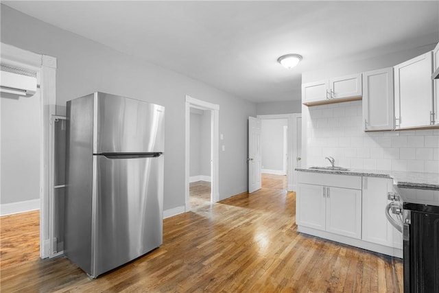 kitchen with decorative backsplash, light stone counters, light hardwood / wood-style floors, white cabinetry, and stainless steel refrigerator