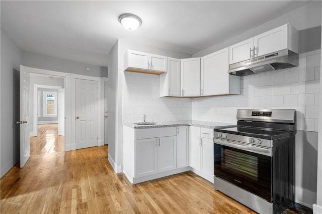 kitchen featuring decorative backsplash, sink, light hardwood / wood-style flooring, stainless steel stove, and white cabinetry