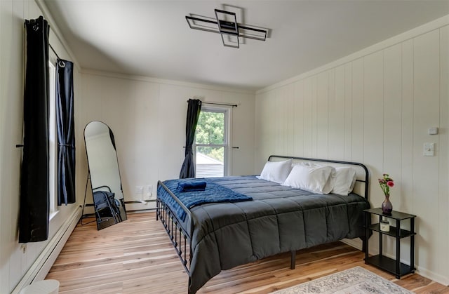 bedroom featuring light hardwood / wood-style floors, baseboard heating, and crown molding