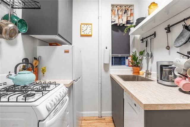 kitchen featuring white appliances, light wood-style flooring, light countertops, gray cabinetry, and a sink