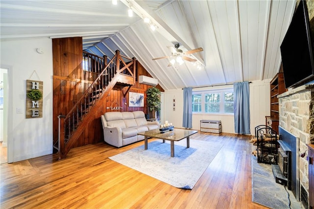 living room with hardwood / wood-style floors, a wall mounted air conditioner, lofted ceiling with beams, ceiling fan, and a fireplace