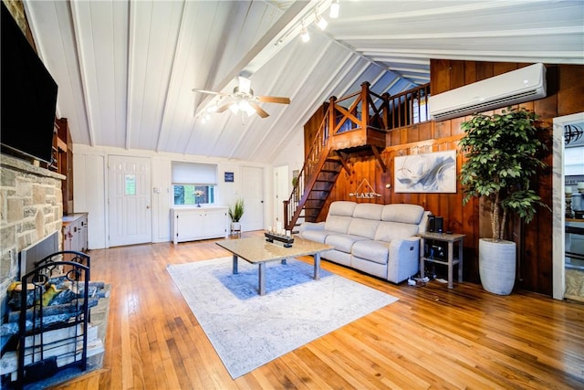 living room with a wall mounted air conditioner, ceiling fan, light hardwood / wood-style floors, lofted ceiling, and wood walls