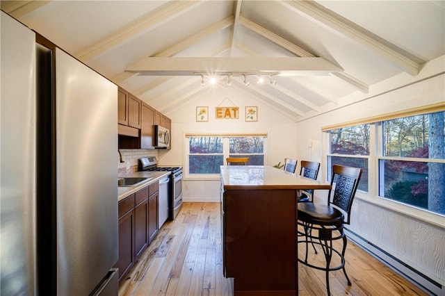 kitchen featuring appliances with stainless steel finishes, a baseboard heating unit, lofted ceiling with beams, a center island, and a breakfast bar area