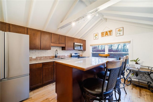 kitchen featuring a kitchen breakfast bar, stainless steel appliances, sink, beam ceiling, and light hardwood / wood-style flooring