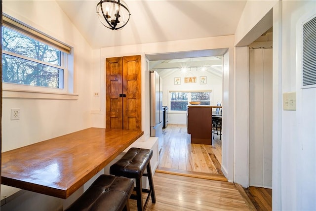 dining space featuring light wood-type flooring, vaulted ceiling, and a notable chandelier