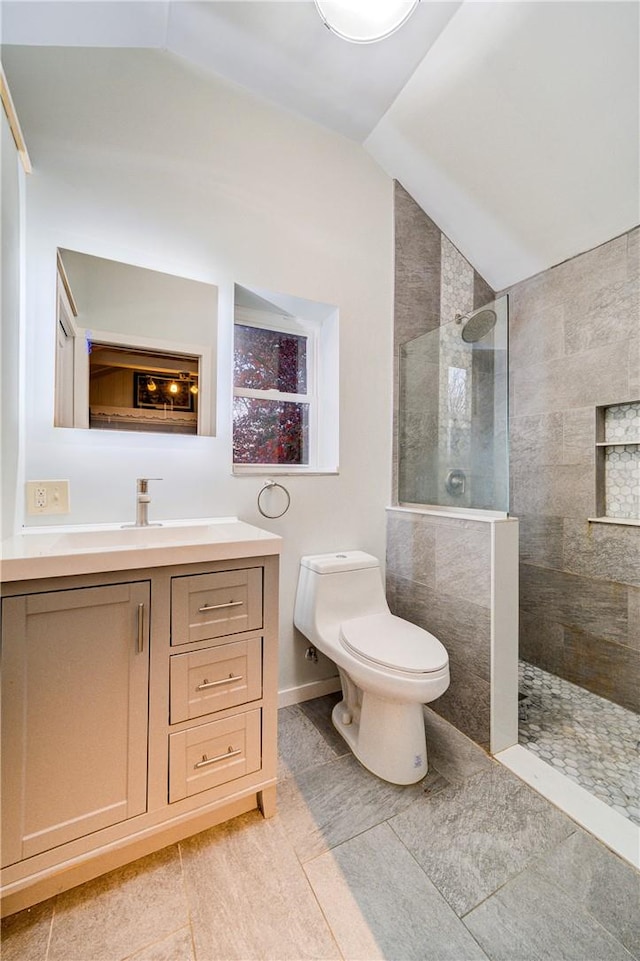 bathroom with vanity, vaulted ceiling, tiled shower, tile patterned flooring, and toilet