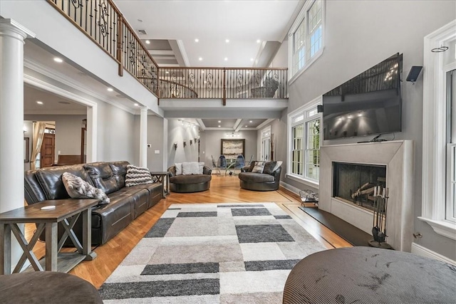 living room featuring light wood-type flooring, ornamental molding, a high ceiling, and ornate columns