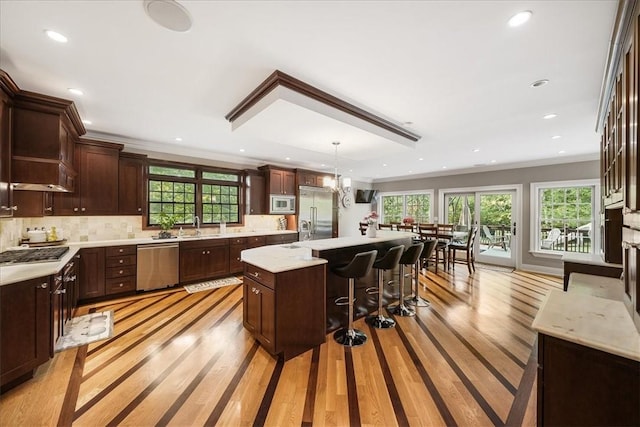 kitchen featuring tasteful backsplash, light hardwood / wood-style flooring, built in appliances, an island with sink, and pendant lighting