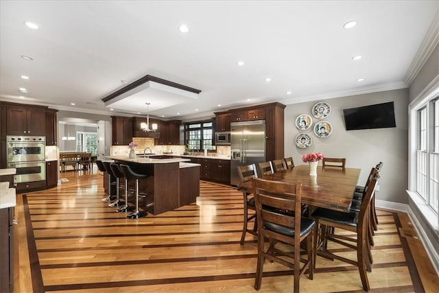 dining room featuring an inviting chandelier, light hardwood / wood-style flooring, crown molding, and sink