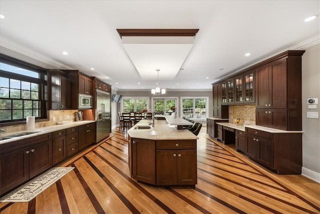 kitchen featuring built in appliances, tasteful backsplash, hanging light fixtures, and light hardwood / wood-style flooring