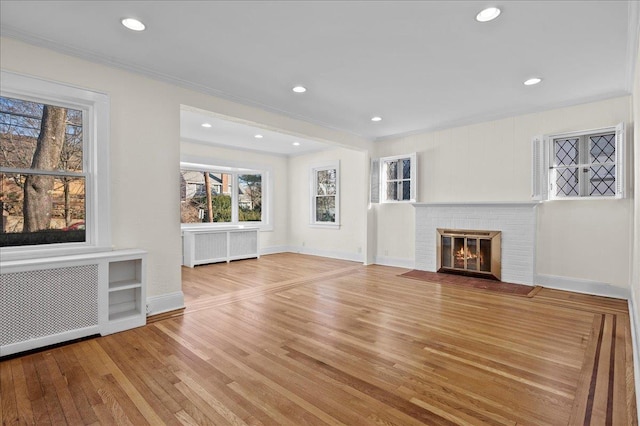 unfurnished living room featuring radiator heating unit, light hardwood / wood-style flooring, crown molding, and a fireplace