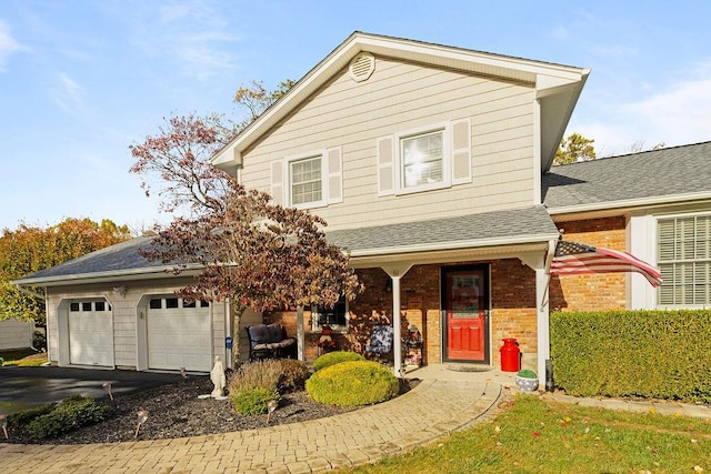 traditional-style house with brick siding, covered porch, a shingled roof, and aphalt driveway