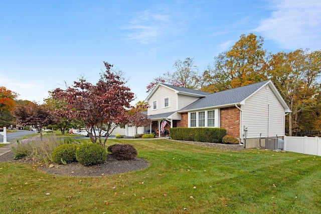 view of front facade with brick siding, cooling unit, a front yard, and fence