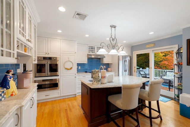 kitchen with under cabinet range hood, visible vents, white cabinets, and freestanding refrigerator