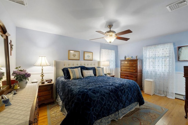 bedroom featuring ceiling fan, visible vents, light wood finished floors, and a baseboard radiator