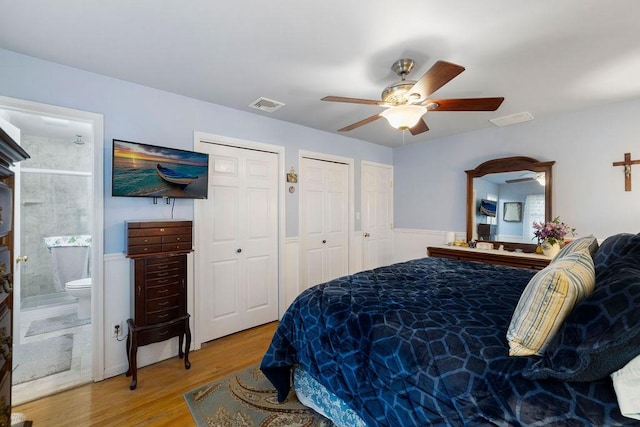 bedroom featuring visible vents, multiple closets, a wainscoted wall, wood finished floors, and a ceiling fan