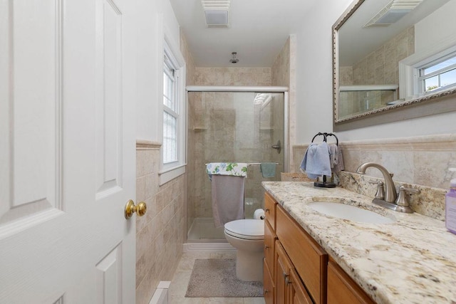 full bathroom with a wainscoted wall, toilet, vanity, a stall shower, and tile walls