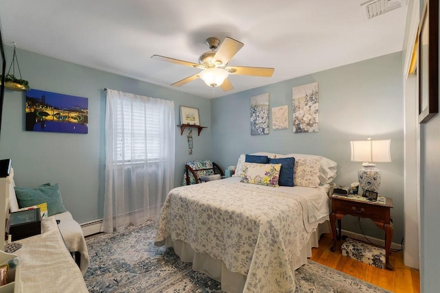 bedroom with visible vents, a ceiling fan, wood finished floors, baseboards, and baseboard heating