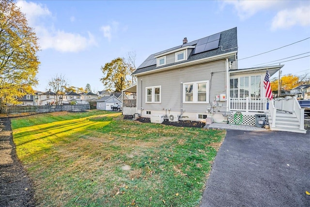 rear view of house featuring a lawn, solar panels, a sunroom, and a wooden deck