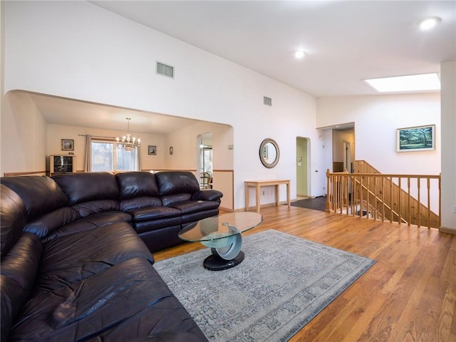 living room with a chandelier, hardwood / wood-style flooring, high vaulted ceiling, and a skylight