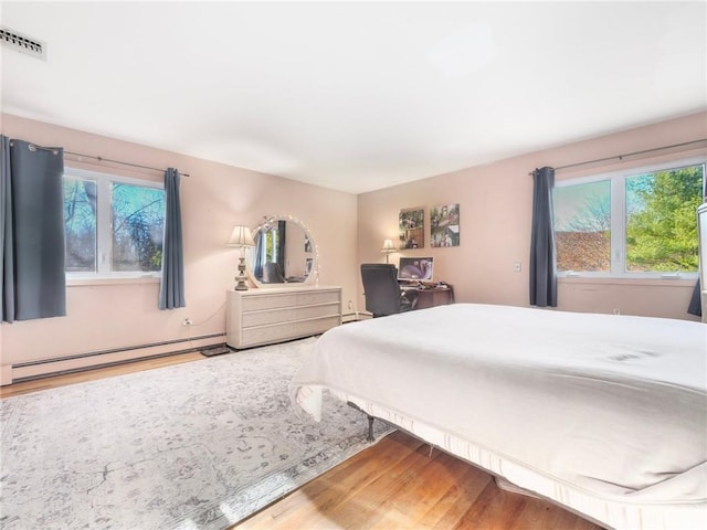 bedroom with hardwood / wood-style floors, baseboard heating, and multiple windows