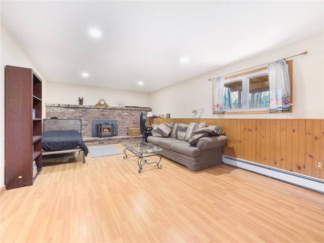 living room featuring baseboard heating, a wood stove, wood walls, and light hardwood / wood-style flooring