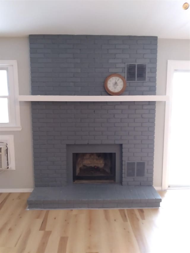 interior details with wood-type flooring, a brick fireplace, and a wall unit AC