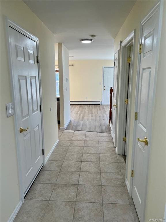 hallway with baseboard heating, light tile patterned flooring, and baseboards