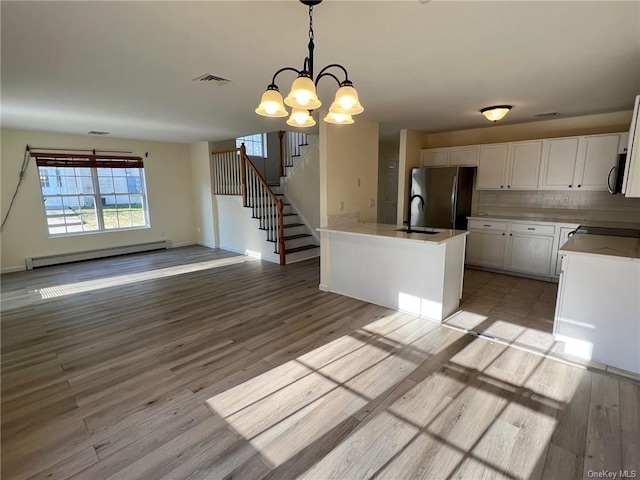 kitchen with a baseboard heating unit, visible vents, white cabinetry, hanging light fixtures, and freestanding refrigerator