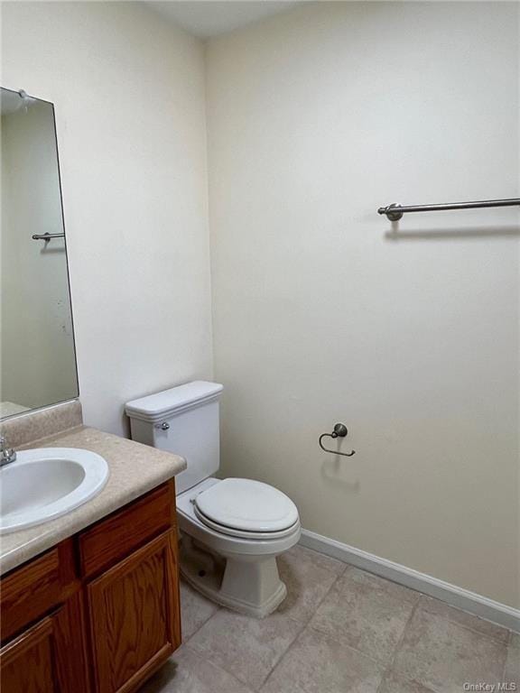 half bathroom with baseboards, vanity, and toilet