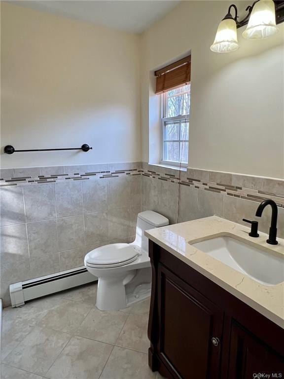 half bathroom with a baseboard radiator, tile patterned flooring, toilet, vanity, and tile walls