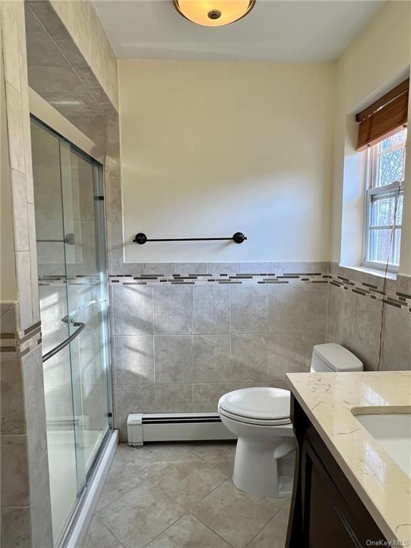 full bathroom with tile walls, a baseboard radiator, toilet, a shower stall, and vanity