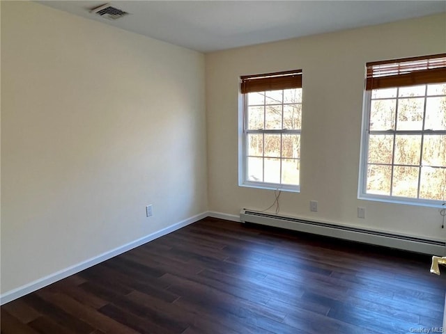 unfurnished room with a baseboard heating unit, visible vents, dark wood finished floors, and baseboards