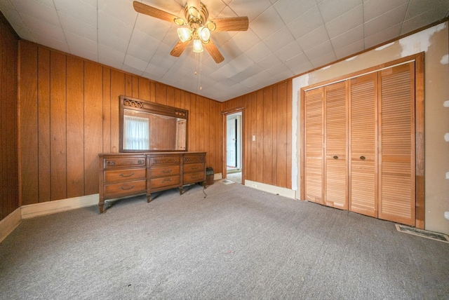 bedroom featuring carpet flooring, ceiling fan, a closet, and wooden walls