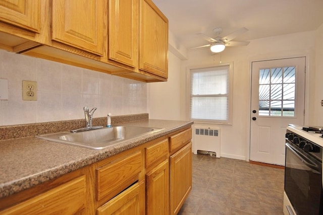 kitchen with stove, backsplash, radiator, sink, and ceiling fan