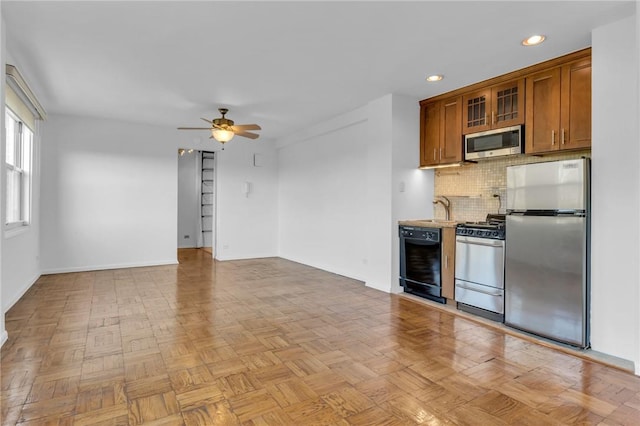 3935 Blackstone Ave Unit 5K, Bronx, NY 10471 - kitchen with stainless steel appliances, brown cabinetry, a ceiling fan, decorative backsplash, and glass insert cabinets