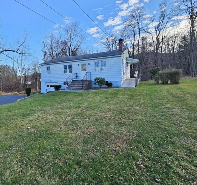 rear view of property with a chimney, aphalt driveway, and a yard