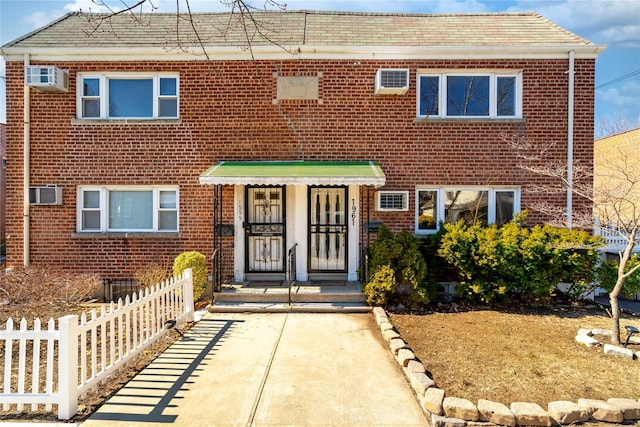 view of front of property with an AC wall unit, brick siding, and fence