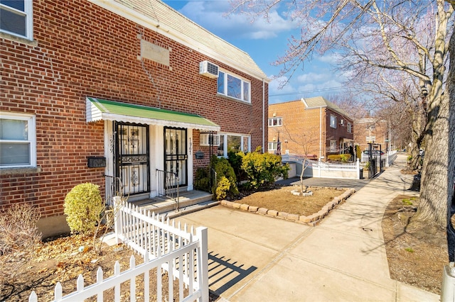 view of front of home with brick siding, a wall mounted air conditioner, and fence