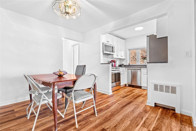 dining area with light wood-type flooring, an inviting chandelier, radiator heating unit, and baseboards