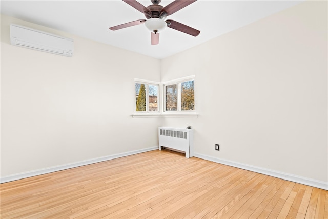 unfurnished room with a wall unit AC, wood-type flooring, radiator heating unit, a ceiling fan, and baseboards