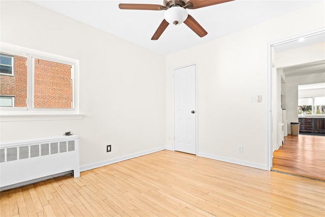 unfurnished bedroom featuring baseboards, ceiling fan, radiator heating unit, and light wood-style floors