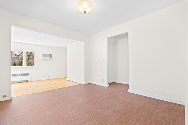 unfurnished room with baseboards, a wall mounted air conditioner, wood finished floors, and radiator