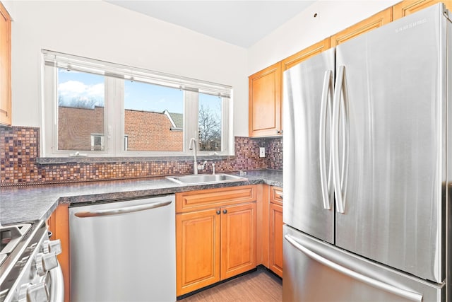 kitchen featuring decorative backsplash, dark countertops, stainless steel appliances, light wood-style floors, and a sink