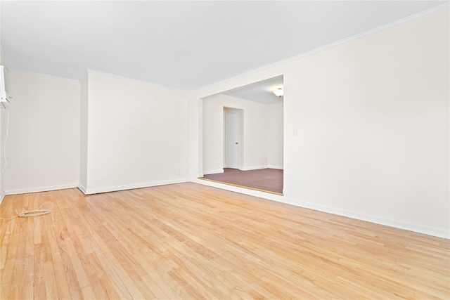 spare room featuring crown molding, baseboards, and light wood-style floors