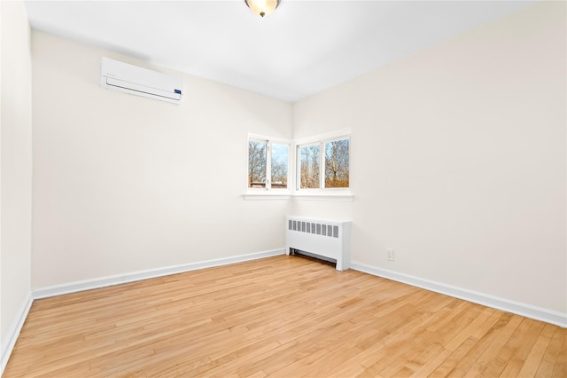 spare room with radiator, light wood finished floors, baseboards, and a wall mounted air conditioner