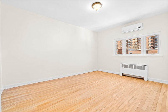 empty room featuring radiator, light wood-type flooring, a wall unit AC, and baseboards