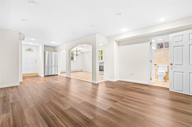 unfurnished living room featuring baseboards, arched walkways, wood finished floors, and recessed lighting