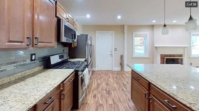 kitchen featuring appliances with stainless steel finishes, tasteful backsplash, light stone counters, pendant lighting, and light hardwood / wood-style flooring